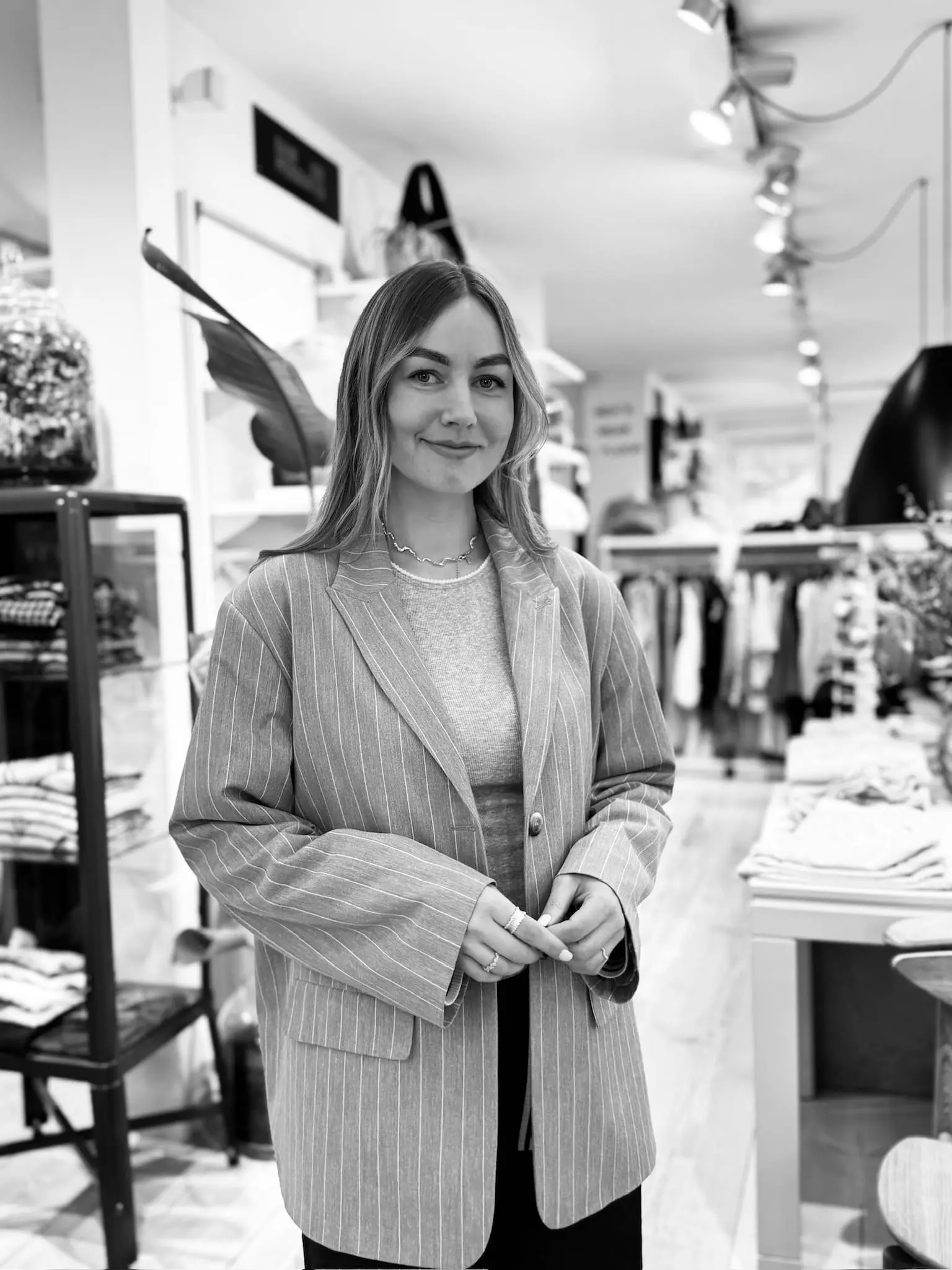 Kvinde med blond hår står i grå stribet blazer i modetøjsbutikken.