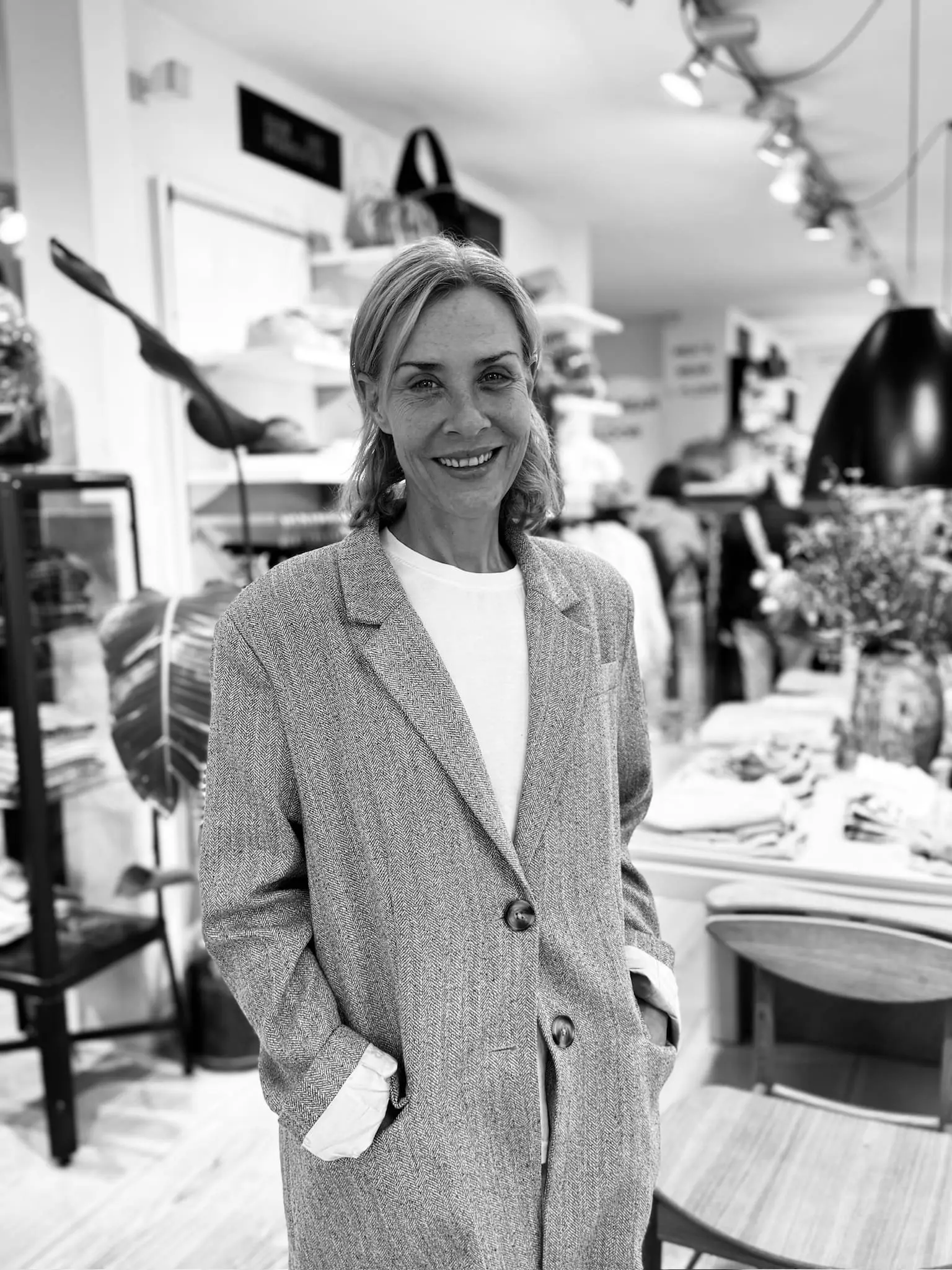 Sort/hvid billede af smilende kvinde i grå blazer i Hinges Hus butik.
