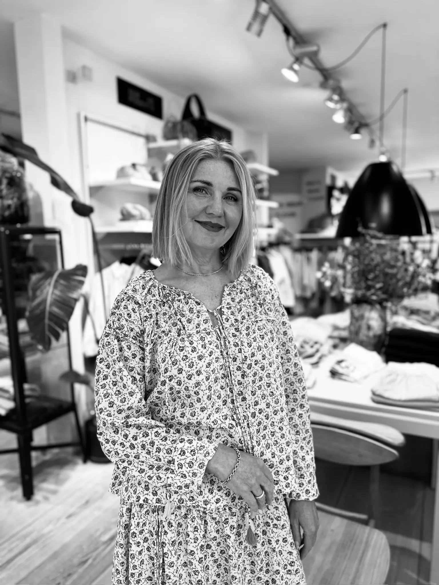 Kvinde med blond hår står i Hinges Hus iført blomstret sæt.