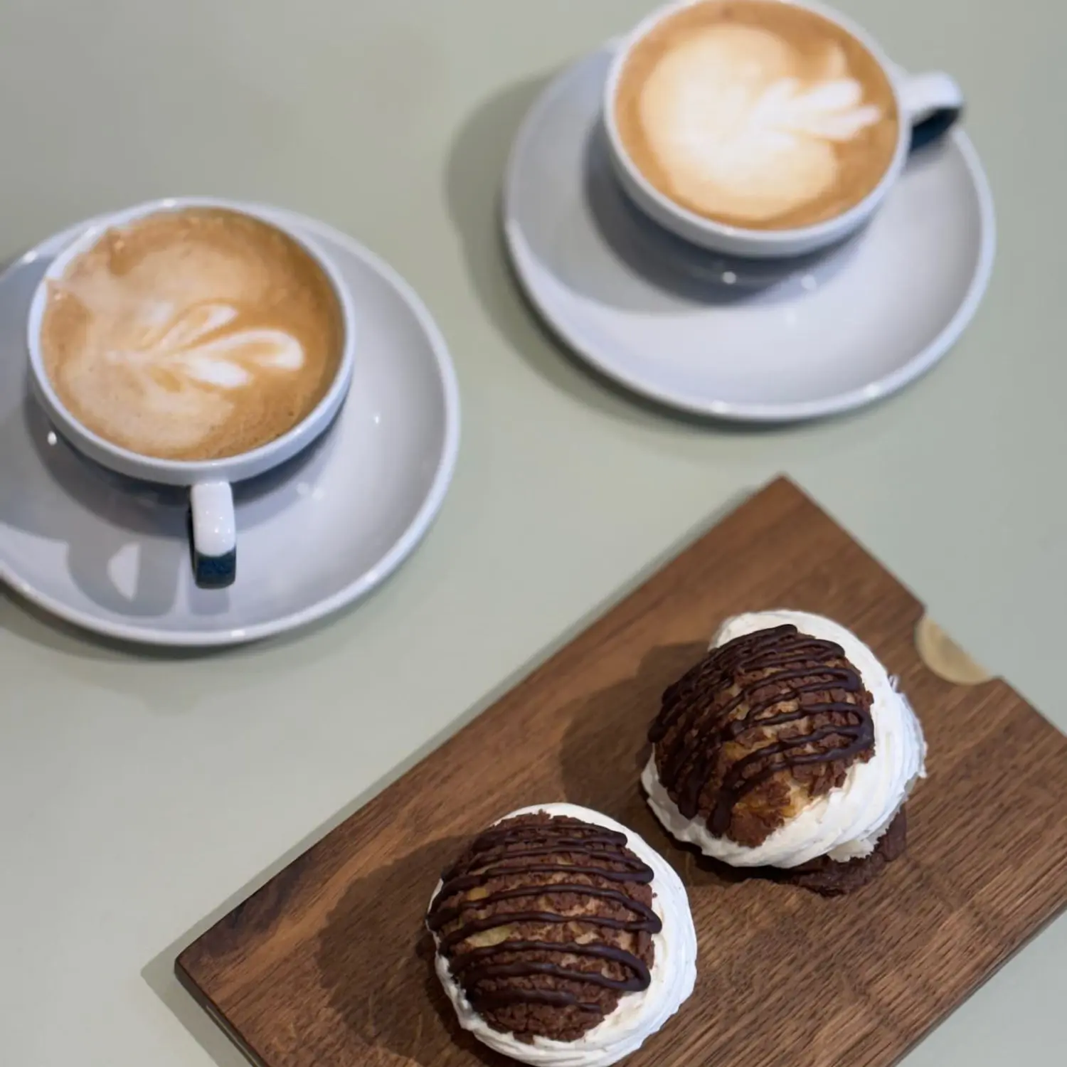 To kopper kaffe latte og lækre kager på et træfad.