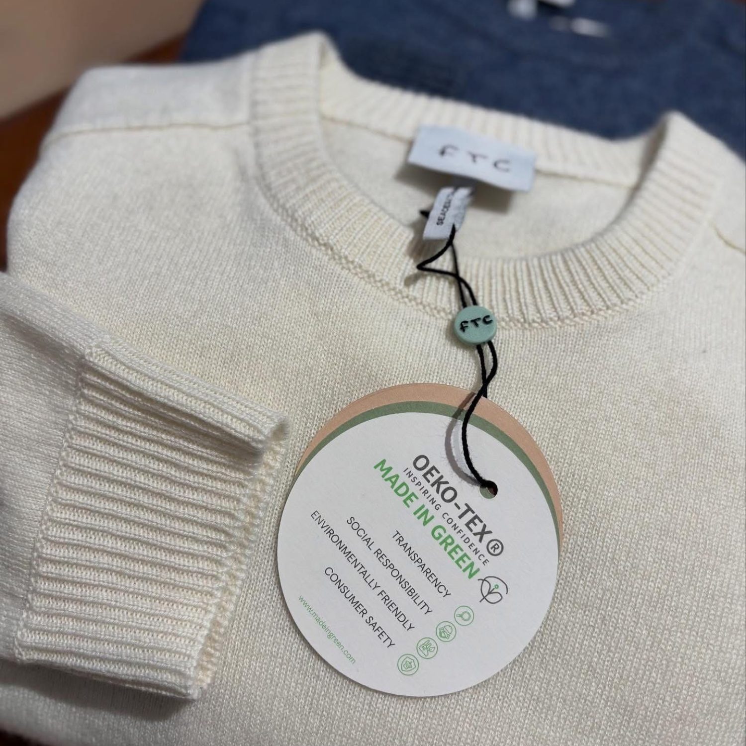 Cremefarvet striktrøje med OEKO-TEX Made in Green mærke, der fremhæver bæredygtighed.